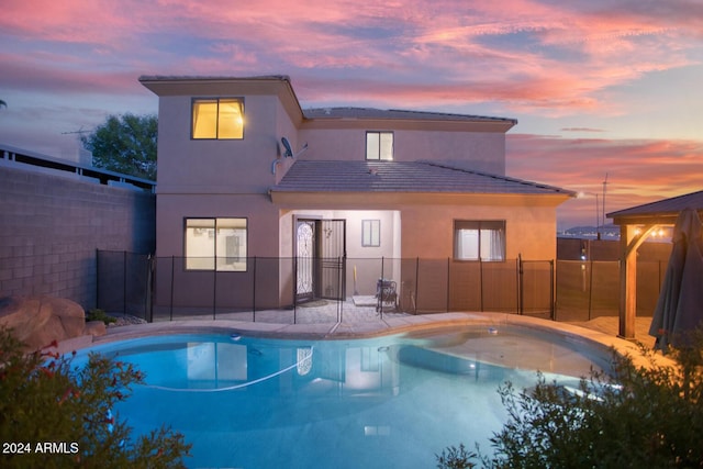 back house at dusk featuring a fenced in pool