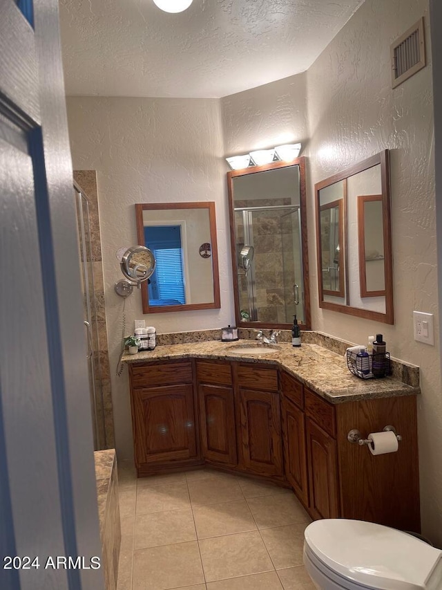 bathroom featuring tile flooring, a textured ceiling, toilet, vanity with extensive cabinet space, and an enclosed shower