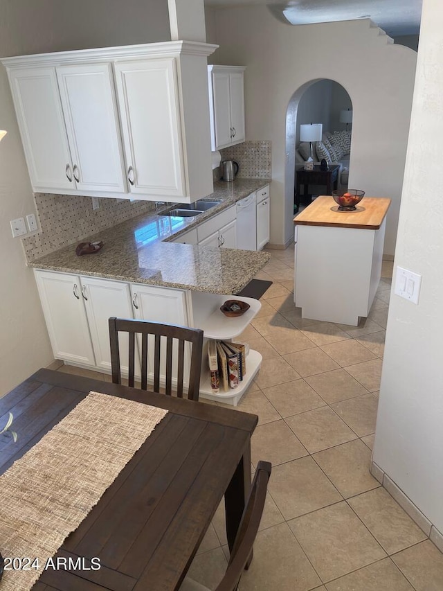 kitchen featuring backsplash, light stone countertops, kitchen peninsula, and white cabinetry