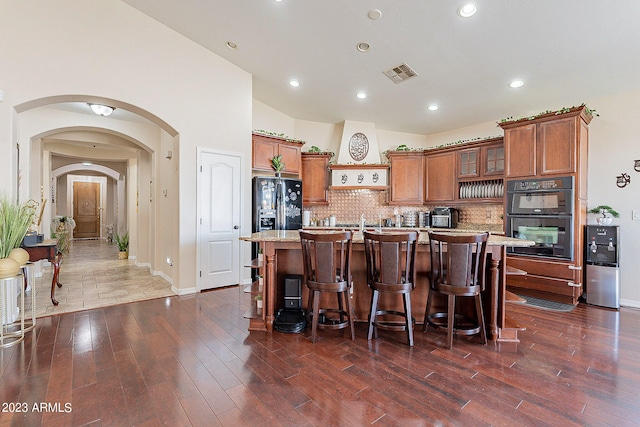 kitchen featuring dark hardwood / wood-style floors, a breakfast bar area, black appliances, and an island with sink