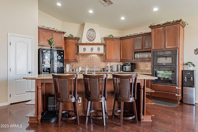 kitchen featuring dark hardwood / wood-style flooring, a center island with sink, light stone counters, and black appliances