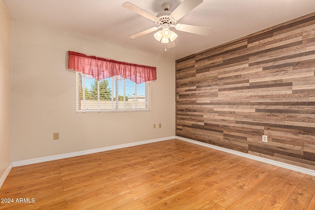 unfurnished room featuring hardwood / wood-style floors, wooden walls, and ceiling fan