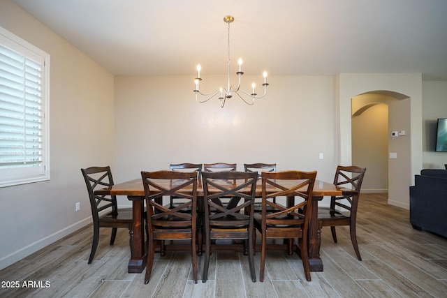 dining space with light wood-style flooring, arched walkways, baseboards, and a chandelier