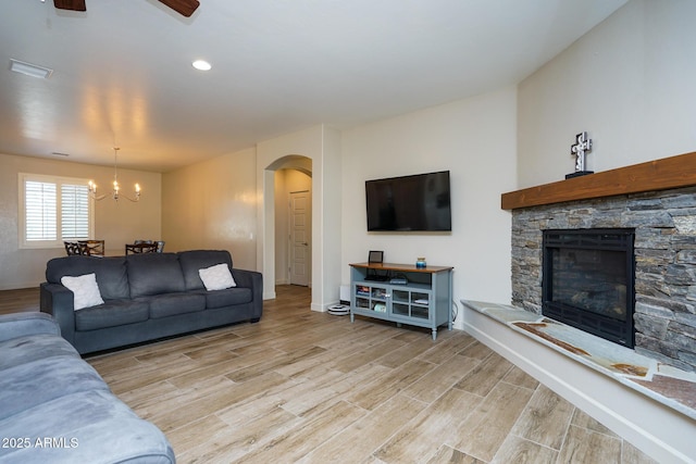 living room featuring arched walkways, baseboards, a stone fireplace, and light wood finished floors