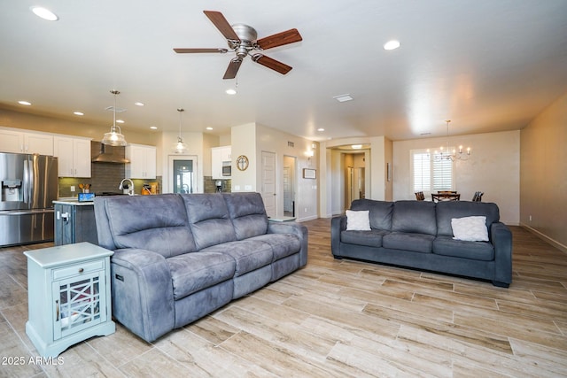 living area featuring ceiling fan with notable chandelier, light wood-type flooring, baseboards, and recessed lighting