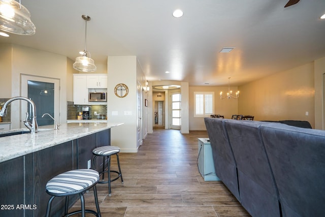kitchen with white cabinetry, stainless steel microwave, backsplash, a sink, and light wood finished floors
