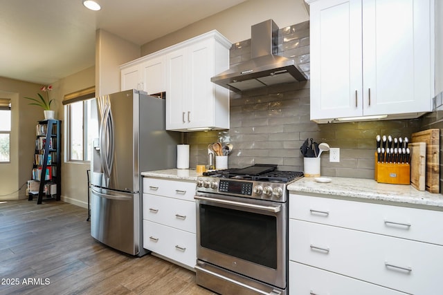 kitchen with wall chimney exhaust hood, wood finished floors, stainless steel appliances, white cabinets, and decorative backsplash