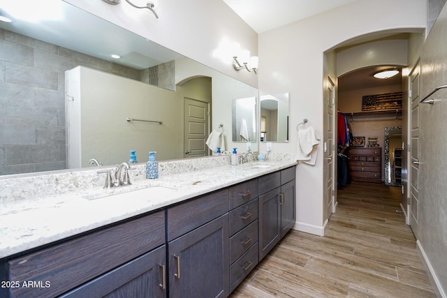 full bath featuring double vanity, a sink, a spacious closet, and wood finished floors