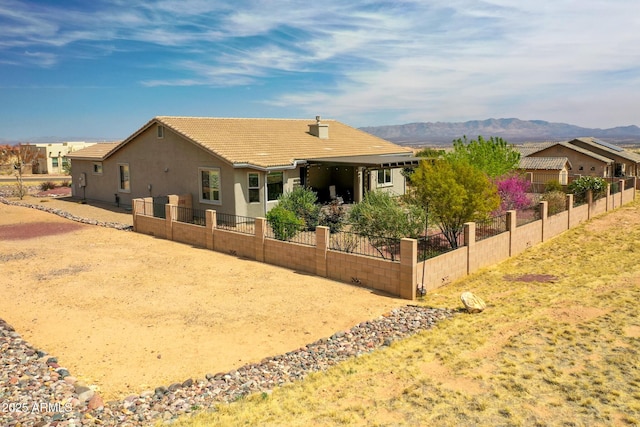 rear view of house featuring a tile roof, a mountain view, stucco siding, and fence
