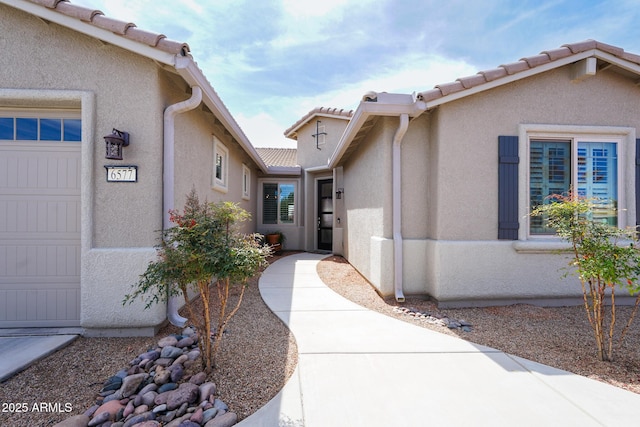 entrance to property with a tile roof, a garage, and stucco siding