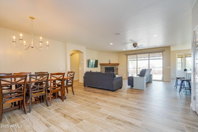 dining space with light wood-type flooring, ceiling fan with notable chandelier, arched walkways, visible vents, and a fireplace