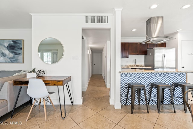 8315 E Devonshire Ave, Scottsdale, AZ 85251 - kitchen featuring freestanding refrigerator, island range hood, a breakfast bar, crown molding, and dark brown cabinets