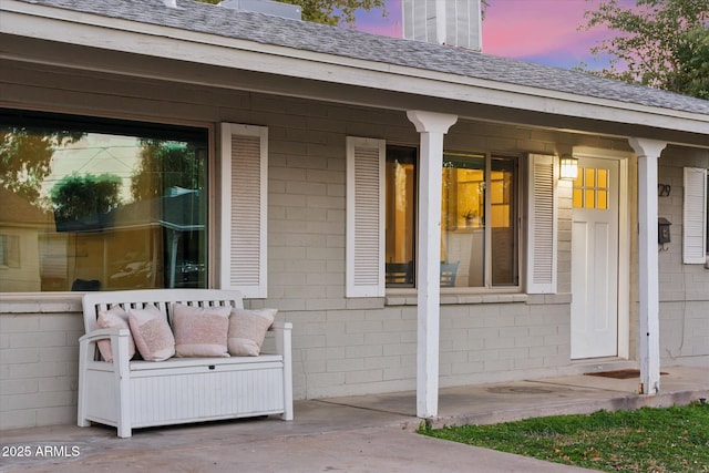 exterior entry at dusk featuring outdoor lounge area, concrete block siding, and roof with shingles