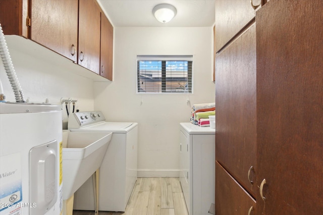 clothes washing area with light wood-type flooring, water heater, cabinet space, baseboards, and washing machine and clothes dryer