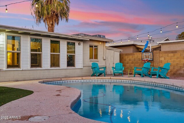 pool at dusk with a patio area, an outdoor pool, and fence