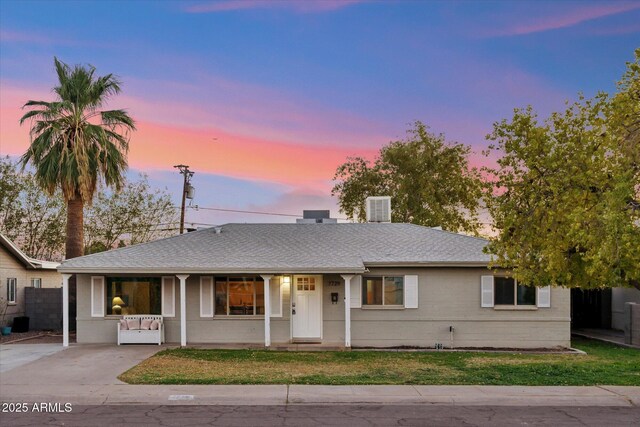 single story home featuring covered porch, a shingled roof, a front yard, and fence