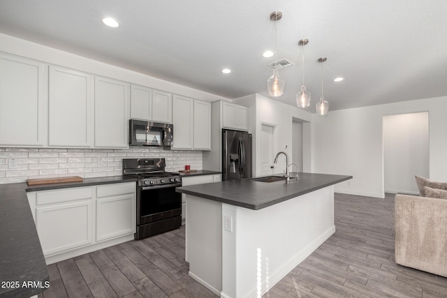 kitchen with stainless steel fridge, decorative backsplash, hanging light fixtures, black range with gas stovetop, and sink