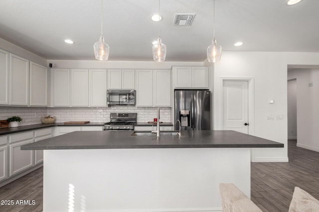 kitchen with appliances with stainless steel finishes, a center island with sink, and decorative light fixtures