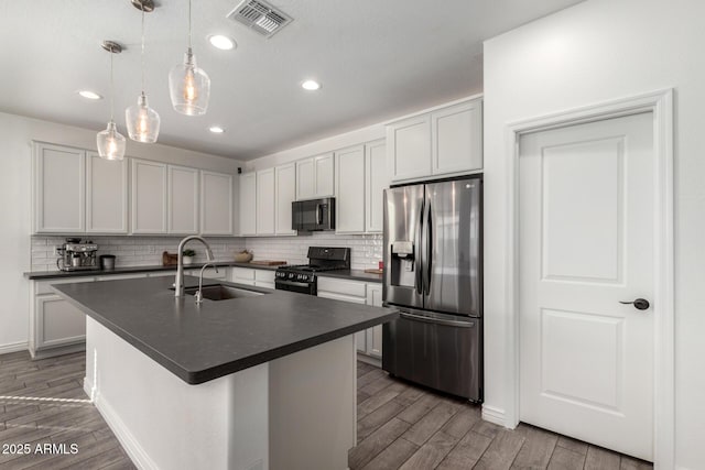 kitchen featuring stainless steel fridge, an island with sink, gas stove, pendant lighting, and sink