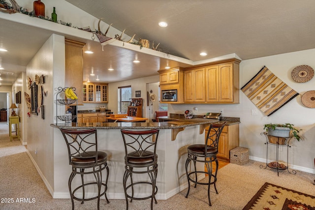 8870 Happy Trl, Show Low, AZ 85901 - kitchen with stainless steel microwave, a kitchen bar, light colored carpet, a peninsula, and dark stone counters