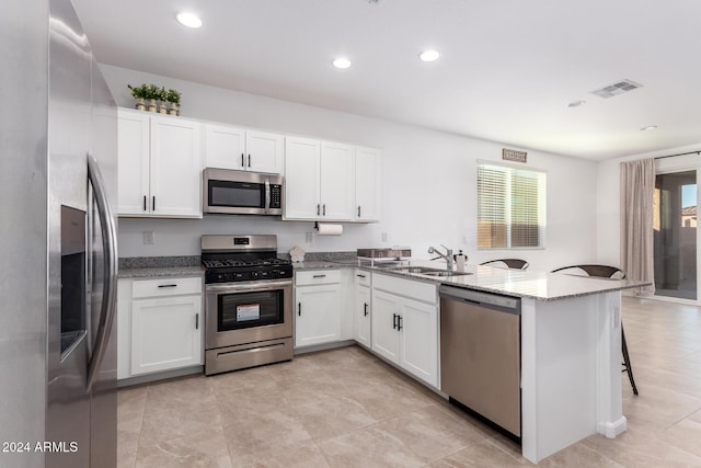 kitchen with kitchen peninsula, light stone countertops, stainless steel appliances, sink, and white cabinets