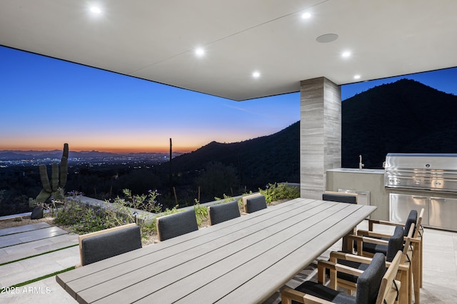 patio terrace at dusk featuring a mountain view, an outdoor kitchen, sink, and grilling area