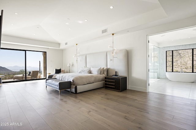 bedroom featuring a raised ceiling, ensuite bathroom, access to outside, and light hardwood / wood-style floors