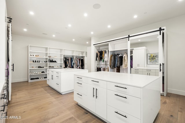 walk in closet with a barn door and light hardwood / wood-style floors