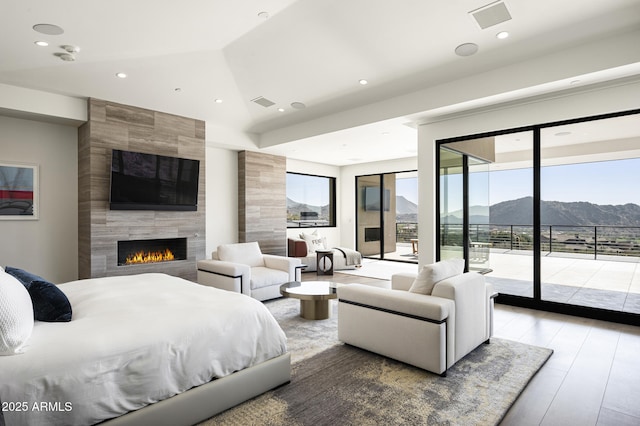 bedroom with a tiled fireplace, hardwood / wood-style flooring, access to outside, and lofted ceiling