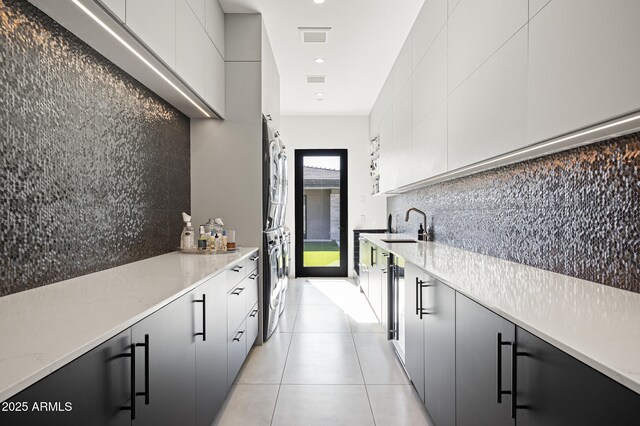 kitchen featuring light tile patterned flooring, sink, stacked washer / dryer, light stone countertops, and decorative backsplash