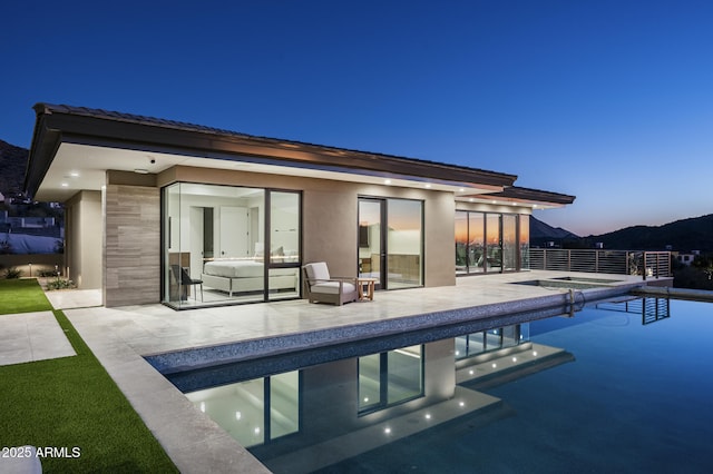 back house at dusk with a swimming pool with hot tub and a patio area