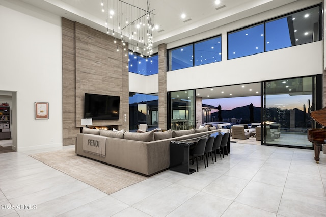 living room featuring an inviting chandelier, a towering ceiling, a fireplace, and light tile patterned floors