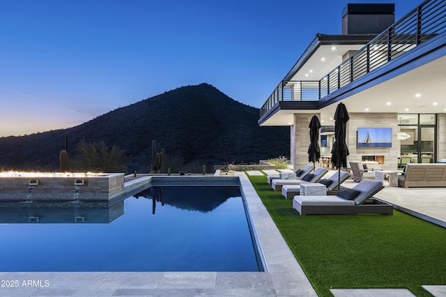 pool at dusk with a mountain view, exterior fireplace, and a patio area