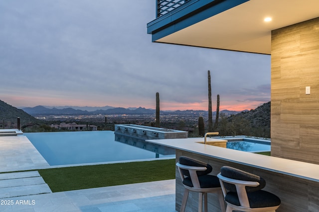 pool at dusk featuring a mountain view and an outdoor bar