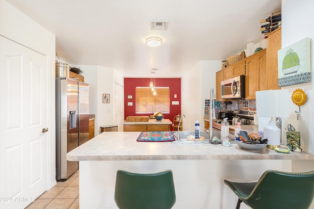 kitchen featuring kitchen peninsula, appliances with stainless steel finishes, a kitchen breakfast bar, pendant lighting, and light tile patterned flooring