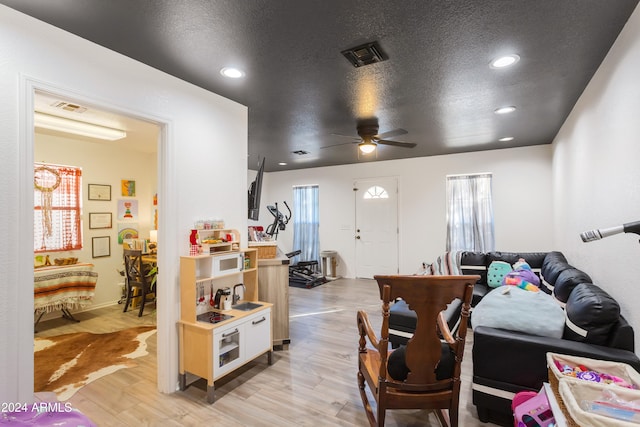 living room featuring ceiling fan, light wood-type flooring, and a textured ceiling