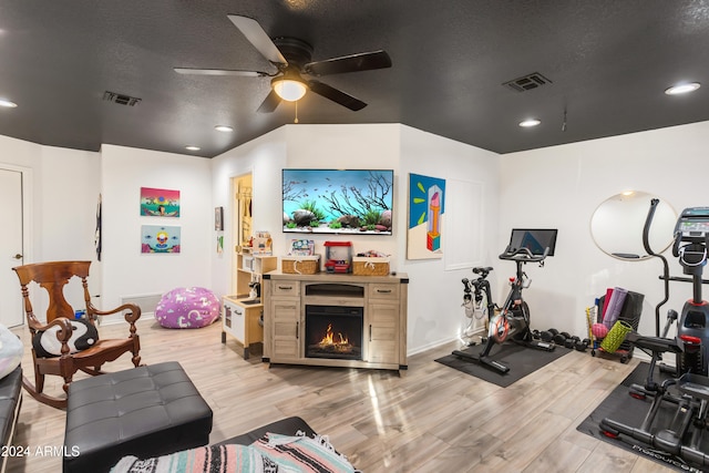 workout room with ceiling fan, light hardwood / wood-style flooring, and a textured ceiling