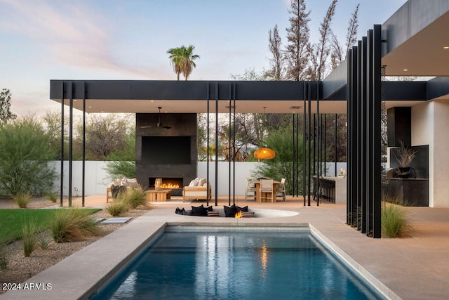 pool at dusk featuring an outdoor fireplace and a patio area