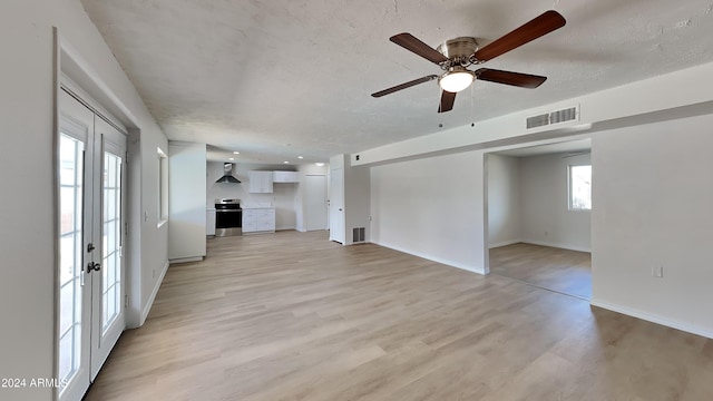 unfurnished living room featuring french doors, a wealth of natural light, ceiling fan, and light hardwood / wood-style flooring