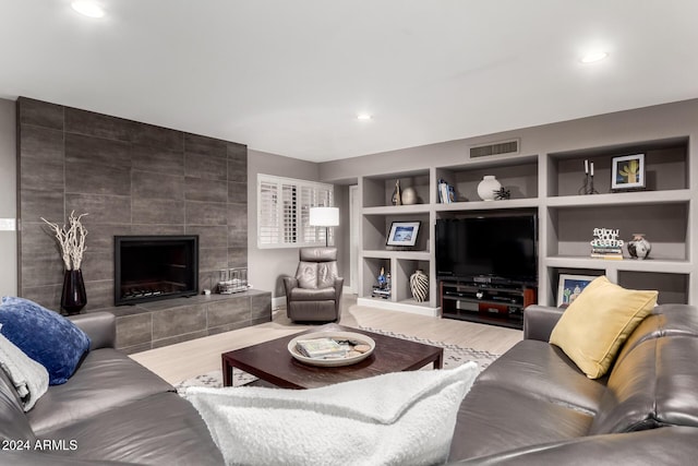 living room featuring a tile fireplace, built in features, and hardwood / wood-style flooring