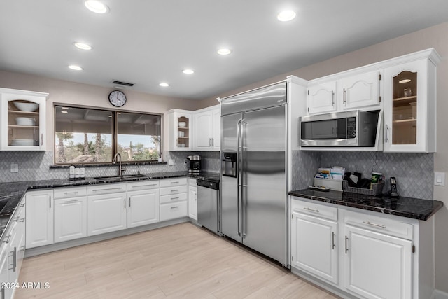 kitchen with built in appliances, white cabinets, sink, and dark stone counters