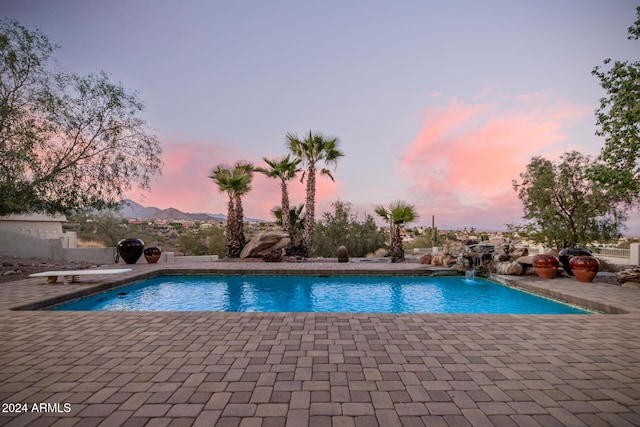 pool at dusk featuring pool water feature, a mountain view, and a patio area