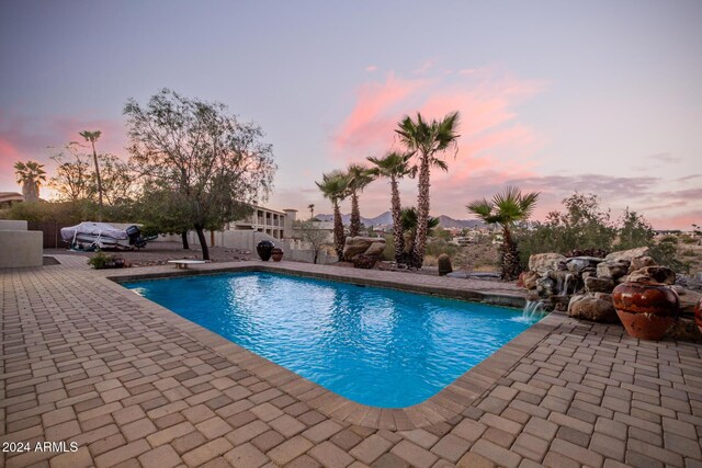 pool at dusk featuring a diving board, pool water feature, and a patio