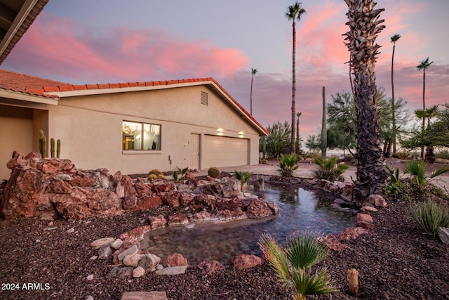 property exterior at dusk with a garage and a garden pond