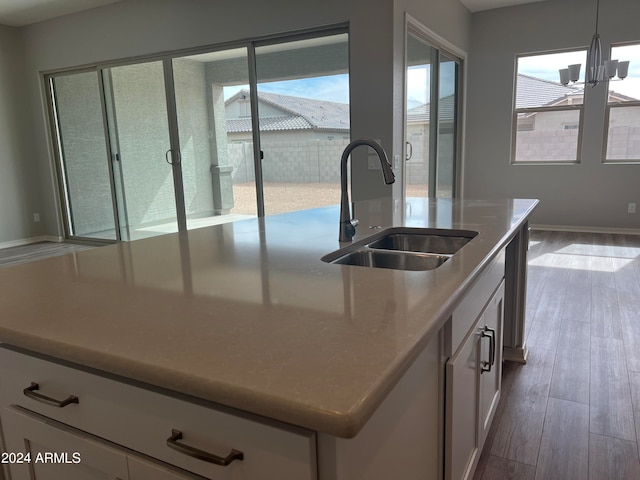 kitchen featuring pendant lighting, sink, white cabinets, light hardwood / wood-style flooring, and a center island with sink