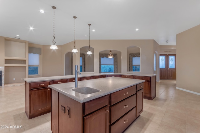 kitchen with light stone countertops, sink, french doors, pendant lighting, and a kitchen island with sink