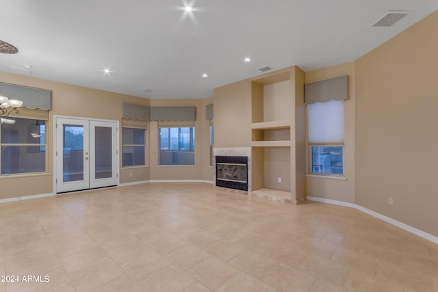 unfurnished living room featuring french doors, built in features, a fireplace, light tile patterned floors, and a chandelier