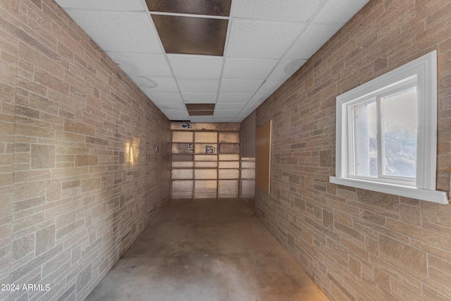 basement with a paneled ceiling and brick wall