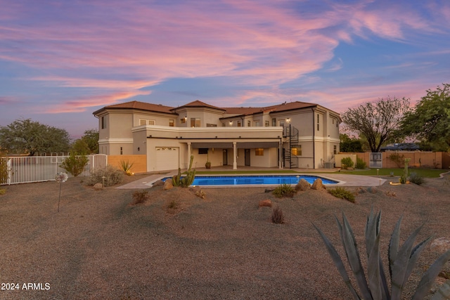 back house at dusk with a fenced in pool and a garage