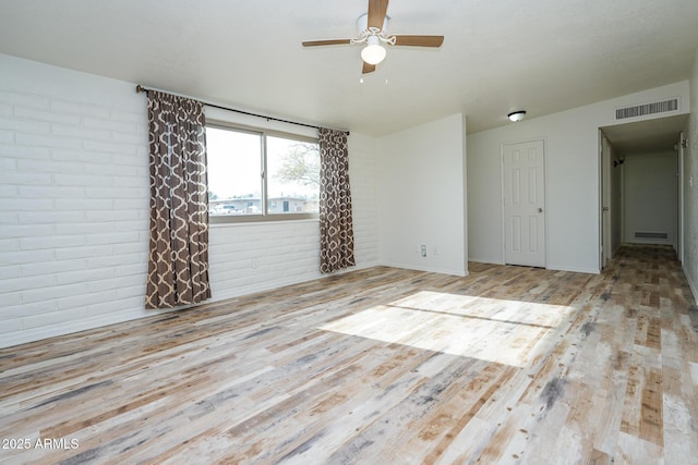 unfurnished room featuring ceiling fan, visible vents, brick wall, and wood finished floors